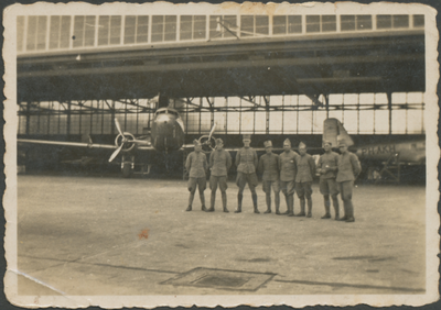 860940 Groepsportret van enkele gemobiliseerde militairen bij een grote hangar met vliegtuigen, vermoedelijk op ...